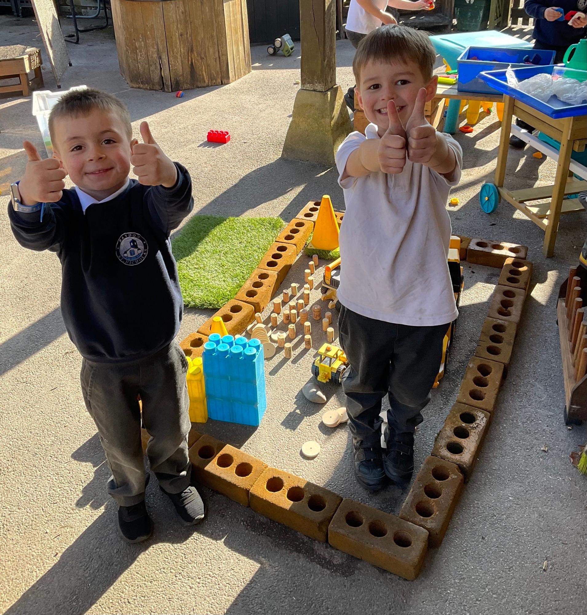 Two pupils with their thumbs up and smiling at the camera outside.